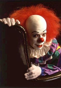 a creepy clown sitting in a chair with his arm around the back of it's head