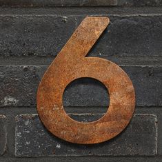 the number five is made out of rusted metal and sits on a brick wall