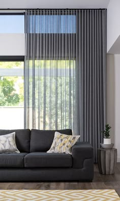 a living room filled with furniture and windows covered in grey drapes next to a plant