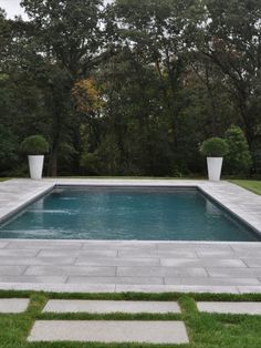 an empty swimming pool in the middle of a lawn with two planters on each side