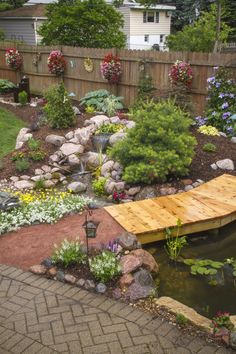 a wooden bridge over a small pond in a backyard area with flowers and plants around it