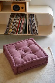 a pink dog bed sitting on top of a rug next to a shelf filled with records