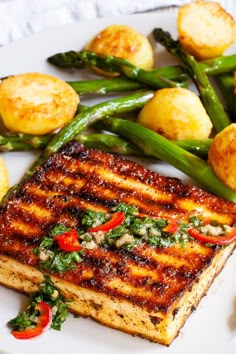 a white plate topped with grilled fish next to asparagus and potato wedges