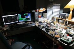 two computer monitors sitting on top of a desk covered in wires and other electronic equipment