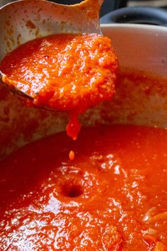 a ladle full of tomato sauce being lifted from a pot