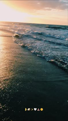 the sun is setting over the ocean with waves coming in to shore and two hearts drawn on the sand