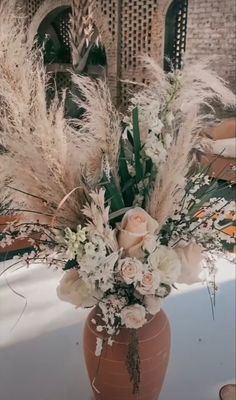 a vase filled with lots of white flowers and greenery on top of a table