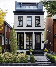 a white house with black windows and steps leading up to the front door is surrounded by landscaping