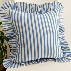 a blue and white striped pillow sitting on top of a chair next to a potted plant