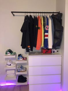 a white dresser topped with lots of clothes and shoes next to a wall mounted coat rack