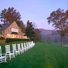 rows of white chairs lined up in front of a large stone house at dusk with the lights on