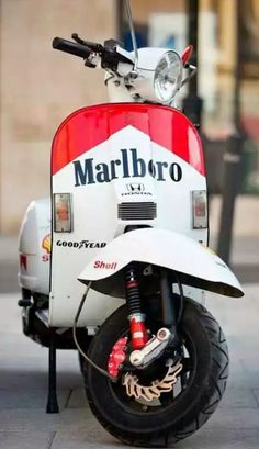 a red and white moped parked on the side of a street next to a motorcycle