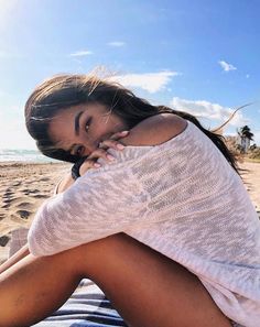 a woman sitting on top of a sandy beach next to the ocean and holding her head