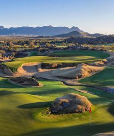 a golf course with mountains in the background and green grass on both sides, surrounded by sand mounds