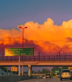 cars are driving on the highway under an orange sky with clouds in the back ground