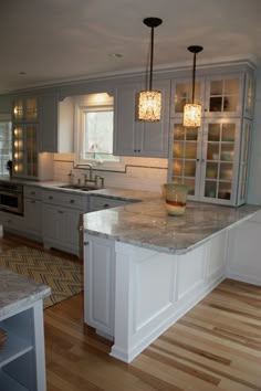 a large kitchen with white cabinets and marble counter tops on hard wood floors in front of an island