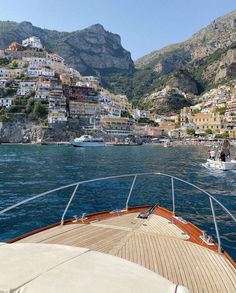 a boat traveling on the water in front of some buildings and mountains with boats passing by