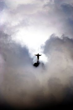 the statue is surrounded by clouds and blue sky with white clouds in the foreground