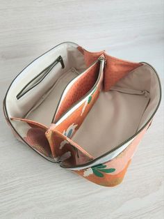 an orange and white flowered purse with zippers on the inside is sitting on a table