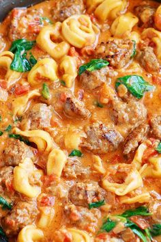 a skillet filled with pasta and meat in tomato sauce, garnished with spinach leaves