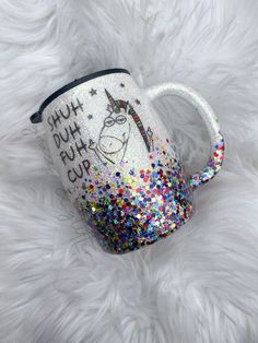 a coffee mug with a unicorn on it sitting on a fluffy white surface, decorated with confetti