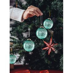 a person is decorating a christmas tree with glass ornaments and red bows on it