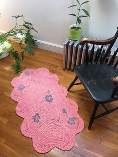 a pink crocheted rug sitting on top of a wooden floor next to a chair