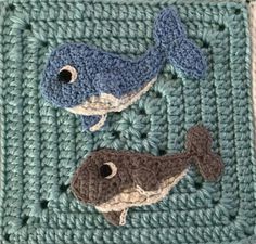 two crocheted whales on a blue square