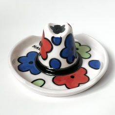 a ceramic hat sitting on top of a white plate with blue, red and green flowers