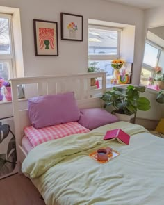 there is a bed with pink and green sheets on it in the room next to two potted plants