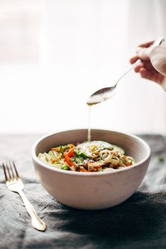 a person is pouring dressing into a bowl with broccoli and carrots in it