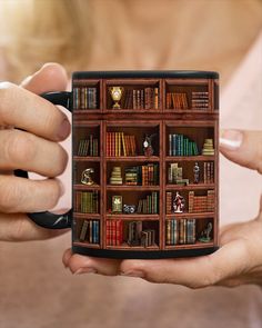 a woman holding a coffee mug with bookshelves on the shelf in front of her