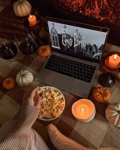 a person sitting in front of a laptop on a table with pumpkins and candles