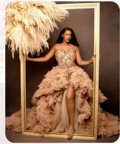 a woman in a dress is holding a frame with feathers on it and posing for the camera