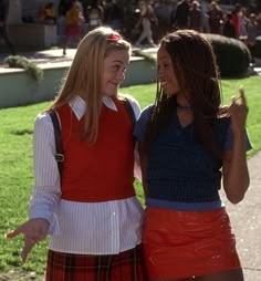 two young women dressed in school uniforms standing next to each other on a sidewalk with people behind them