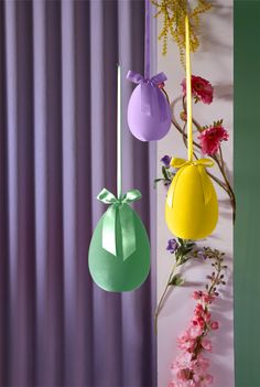 three different colored vases hanging from the side of a wall with flowers in front of them