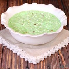 a white bowl filled with green soup on top of a wooden table next to a napkin