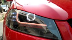 the front end of a red car with its hood up and headlight turned on