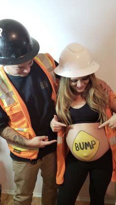 a man and woman in hardhats standing next to each other holding a pregnant bump