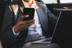 a man sitting in the back seat of a car looking at his cell phone and laptop