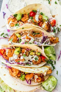 three tacos with shrimp, lettuce and tomatoes