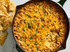 a casserole dish with cheese and tortilla chips on the side next to it