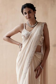 Ivory saree with zari thread, cutdana, sequin embroidery in floral pattern on border. Paired with sleeveless embroidered blouse.
Components: 2
Pattern: Embroidery
Type Of Work: Zari Thread, Cutdana, Sequin, Floral
Neckline: Leaf neck
Sleeve Type: Sleeveless
Fabric: Pure Georgette
Color: Ivory
Other Details: 
Back deep square neck
Pearl drops on pallu
Occasion: Reception - Aza Fashions Ivory Sari, Floral Thread Embroidery, Stylish Saree, Blouse Yoke, Ethnic Suit, Border Saree, Desi Style, Stylish Sarees, Blouse For Women