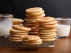 a stack of cookies sitting on top of a wooden table next to milk and glasses