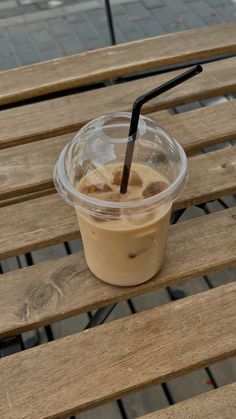 a plastic cup sitting on top of a wooden bench next to a black straw in it