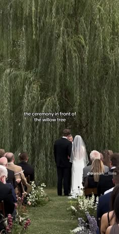 the ceremony in front of this willow tree is filled with flowers and people are standing under it