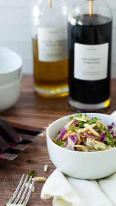 a white bowl filled with salad next to two bottles of wine on a wooden table