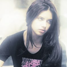 a woman with long brown hair wearing a victoria secret t - shirt and looking at the camera