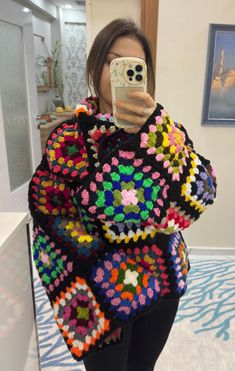 a woman taking a selfie in front of a mirror wearing a colorful crocheted sweater