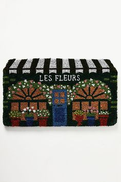 a door mat with an image of a flower shop on the front, and words les fleurs above it